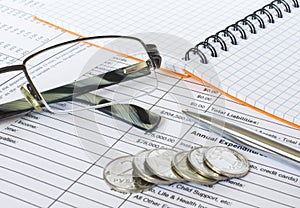 Pen on financial and accounting reports with coins stacks, glasses and calculator in background