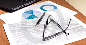 A pen and glasses in black frames on bright graphs and diagrams near the computer. Business concept