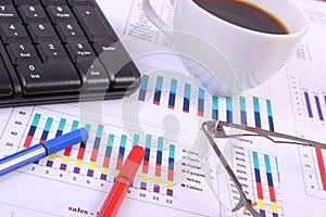 Pen, glasses, computer keyboard and cup of coffee on financial graph, business concept