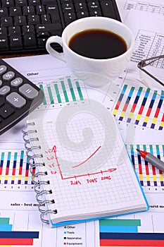 Pen, glasses, computer keyboard and cup of coffee on financial graph, business concept