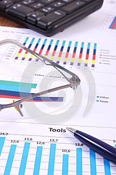 Pen, glasses and computer keyboard on financial graph, business concept