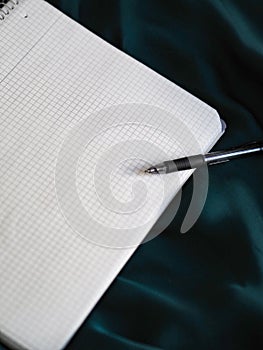 Pen and graphing paper on a shiny blue fabric surface, vertical shot