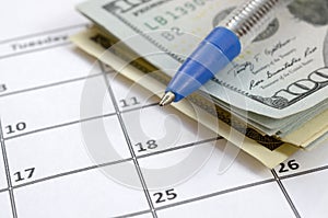 Pen and many hundred US dollar bills on calendar page close up