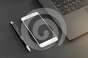 Pen, mobile phone, and laptop keyboard on gray / black desk - view from above