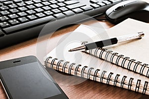 Pen on notebook with computer keyboard, mouse and cell phone