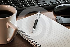 Pen on notebook with computer keyboard, mouse and cell phone