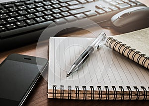 Pen on notebook with computer keyboard, mouse and cell phone