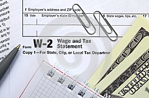 The pen, notebook and dollar bills is lies on the tax form W-2 W