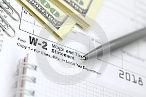 The pen, notebook and dollar bills is lies on the tax form W-2 W