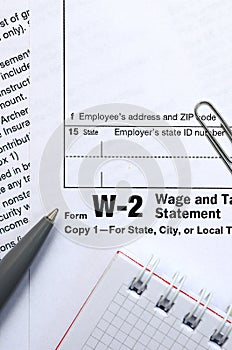 The pen, notebook and dollar bills is lies on the tax form W-2 W