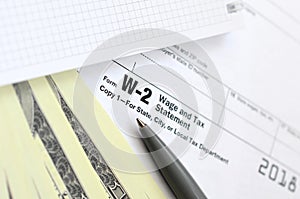 The pen, notebook and dollar bills is lies on the tax form W-2 W