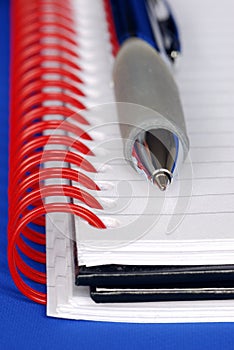A pen and a notebook with red binder