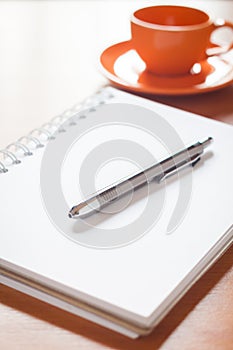 Pen on open blank white notebook with coffee cup on the desk