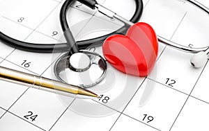 Pen pointing on calendar with stethoscope and red heart. Date for medical examiner