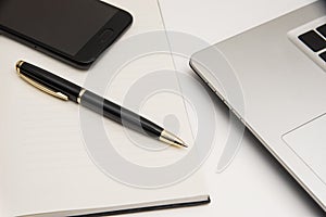 Pen smartphone notebook and laptop on white background