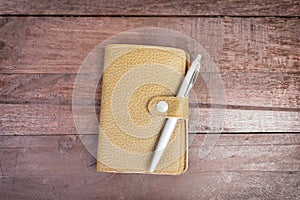 Pen on top of yellow organizer with leather cover on wooden background.