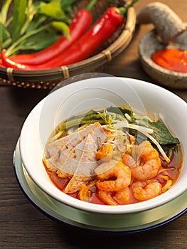 Penang Prawn Mee soup with pork, vegetables, red chili and shrimp in white bowl