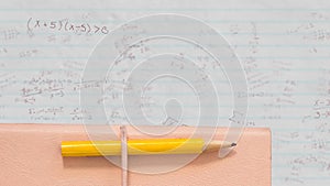 Pencil and book against mathematical equations on white lined paper