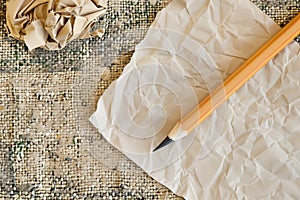 pencil with a chewed end next to crumpled blank paper on a textured rug