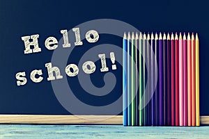 Pencil crayons and text hello school written on a chalkboard