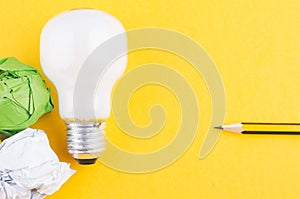 Pencil, crumple paper and bulb over yellow background