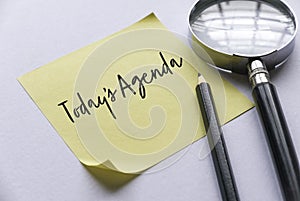 Pencil, magnifying glass and yellow memo note written with Today's Agenda on white background
