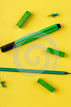 Pencil and marker, chalks of green color and clips, on a yellow background. Top view.