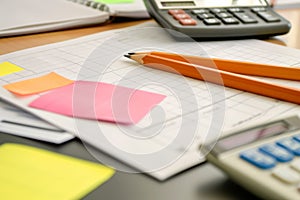 pencil and paper on a desk with sticky notes and a calculator beside