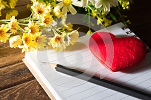 Pencil with red heart on book and flowers