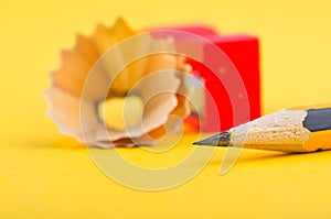 Pencil with it shavings and sharpener over yellow background