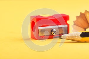 Pencil with it shavings and sharpener over yellow background