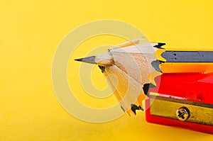Pencil with it shavings and sharpener over yellow background