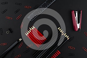 Pencils in black and red, stapler, red and black clips, ruler and knife  on a black background
