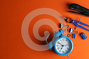 Pencils, blue alarm clock, compass, ruler and stapler on an orange background