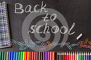 Pencils, clips, notebook and the title Back to school written by white chalk on the black school chalkboard