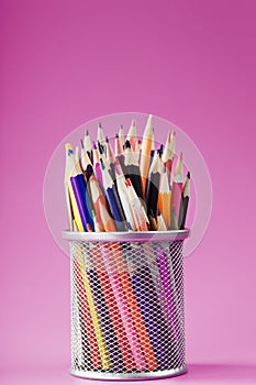 Pencils of different colors in a glass on a pink background