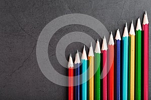 Pencils of different colors in a row on a black textured background.