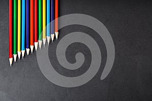 Pencils of different colors in a row on a black textured background.