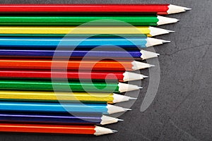 Pencils of different colors in a row on a black textured background.