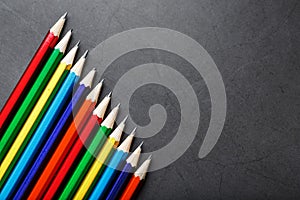 Pencils of different colors in a row on a black textured background.