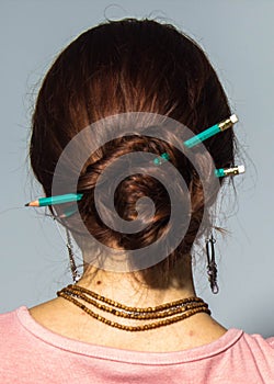 Pencils in head hair updo.  back shot of brunet woman with two green pencils  in her hair.