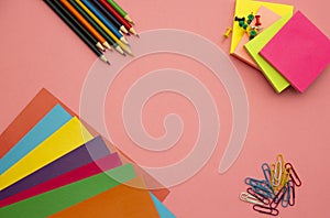 Pencils, multicolored papers and paper clips on a pink background