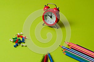 Pencils, pens, push pins and clock on green designer paper