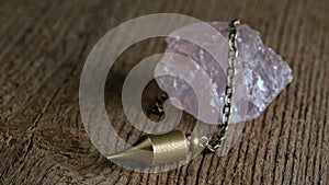 The pendulum on a chain with a natural crystal on a background of wood texture.