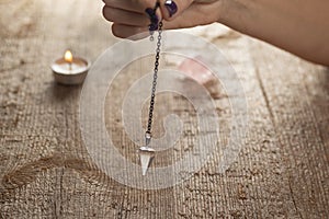 Pendulum on a chain with a natural crystal on a background of wood texture with burning candles. photo