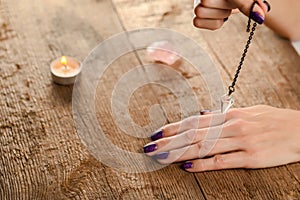 The pendulum on a chain with a natural crystal in hands on a background of wood texture