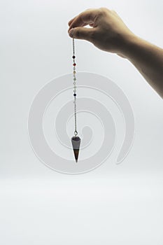 Pendulum dowsing on an isolated white background with a seven colored chakra crystal point