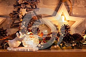 Penguin next to a candle on a mantlepiece with Christmas pinecone garland and golden leaf fairy lights