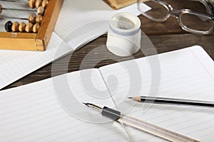 A penholder with a pen, a pencil, an inkwell, glasses and abacus lie on an old wooden table. View from above.