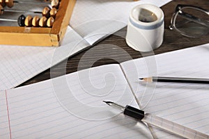 A penholder with a pen and a simple pencil lie on an open notebook. View from above. Close-up.